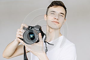 A young man holds a photo camera in his hand and looks straight. Isolated gray background photo