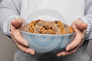 A young man holds a plate with homemade cookies with raisins, chocolate, nuts. Breakfast. Close.