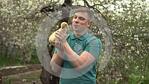 A young man holds a real duckling in his arms. A man in the garden with a bird.