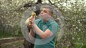 A young man holds a real duckling in his arms. A man in the garden with a bird.