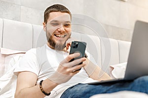 young man at home on the couch with a laptop and phone