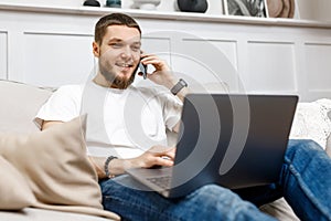 young man at home on the couch talking on the phone and looking at the laptop