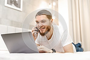 young man at home on the couch talking on the phone and looking at the laptop