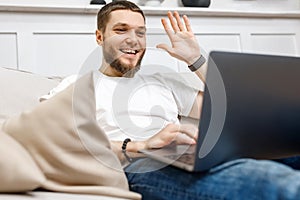young man at home on the couch talking by video with a laptop