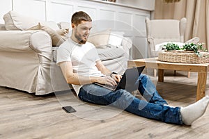 young man at home on the floor near the sofa working on a laptop with a phone