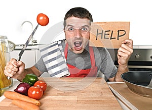 Young man at home kitchen in cook apron desperate in cooking stress