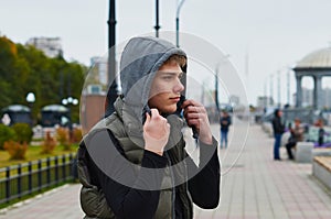 Young man in a hood on the embankment. Rotunda and street lamps. Blur the background.
