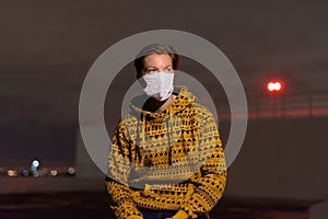 Young man with hoodie wearing mask while thinking outdoors during stormy weather at night