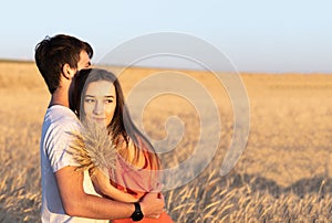 Young man hugging his girlfriend on sunset in wheat field. Copy space, love, togetherness concept.