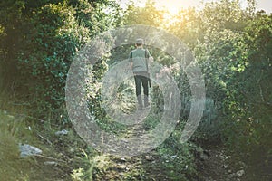 Young man hunting in autumn time with back lighting - Hunter walking in a path in the wood - Hunting and hobby concept - Soft