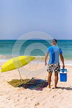 Young man with ice bar cooler under solar umbrella on a beach ne