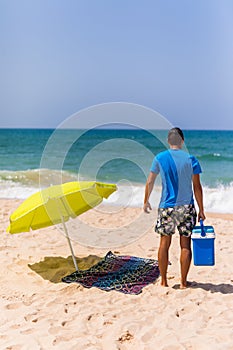 Young man with ice bar cooler under solar umbrella on a beach ne