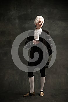 Young man in image of Amadeus Mozart, medieval person isolated on dark green vintage background. Retro style, comparison