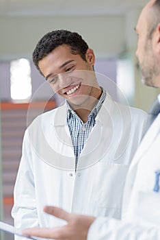 Young man in industrial white coat reading clipboard with supervisor