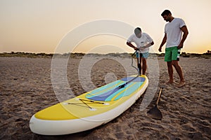 Young man inflating paddle sup board on the beach at sunrise