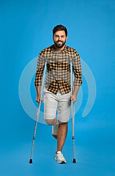 Young man with injured leg using axillary crutches on light blue background