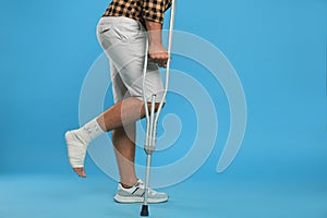 Young man with injured leg using axillary crutches on light blue background, closeup. Space for text