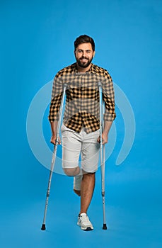 Young man with injured leg using axillary crutches on light blue background photo