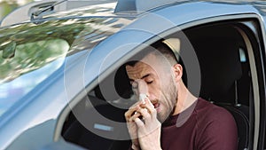 Young man inside car. Sick ill hipster sneezing into white tissue and suffer. Wipe nose and eyes from tears. Coronavirus