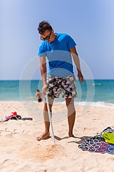 Young man install in sand solar umbrella on a beach