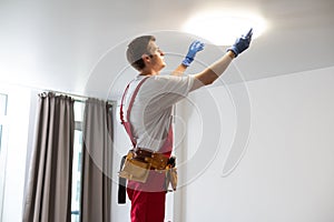 Young man installing ceiling lamp on stepladder in kitchen