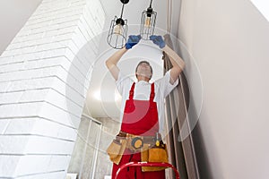 Young man installing ceiling lamp on stepladder in kitchen