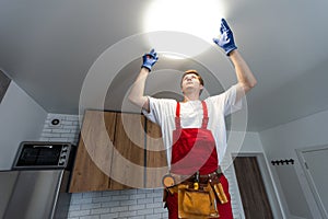 Young man installing ceiling lamp on stepladder in kitchen