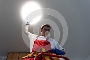 Young man installing ceiling lamp on stepladder in kitchen