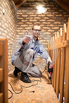 Young man installing flooring in the attic, showing thumbs-up and looking directly at camera