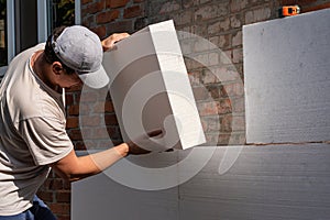 A young man insulates the walls of an apartment building