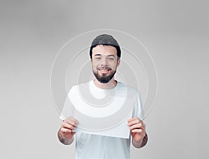 Young man isolated over background. Bearded guy in white shirt hold blank page in hands and smile on camera. Alone in