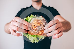 Young man isolated over background. Cut view of guy holding bun with green lettuce. Tasty delicious sandwich. Ready to