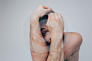 Young man isolated over background. Disroder and unbalanced human cover face with hands and look through them on camera photo