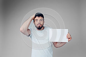 Young man isolated over background. Emotional worried guy hold blank page in hand. Alone in room posing on camera. Badly