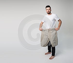 Young man isolated over background. Guy with big large pants in hands posing on camera. Cover them his legs. Facial