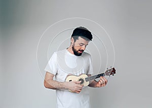 Young man isolated over background. Stand alone and play akulele. Practicing for being better musician. Small guitar in