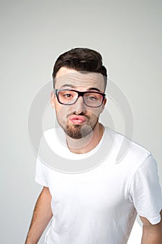 Young man isolated over background. Strange weird guy look stright through glasses and hold lips in kiss mode. Stand