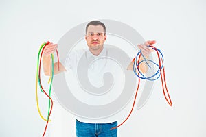 Young man isolated over white background. Confused guy hold colorful electrical cords. Good for reusing and recycling