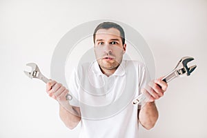 Young man isolated over white background. Confused guy hold two wrenches in hands and posing on camera. Repair man or