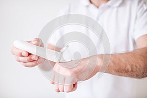 Young man isolated over white background. Cut view of male`s hands getting some hydrationcream out of bottle