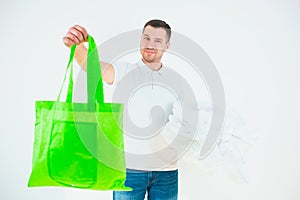 Young man isolated over white background. Guy hold green eco bag in one hand and planty white plastic bags in another