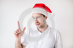 Young man isolated over white background. Guy point up and look with passion on camera. Wear Santa hat Christmas time