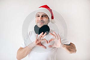Young man isolated over white background. Guy in santa hat hold fingers in heart shape position. Love cheerful emotions