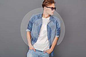 Young man in jeans jacket and sunglasses studio isolated on grey looking aside cool