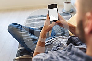 Young man in jeans looking at smartphone screen sitting on sofa at home