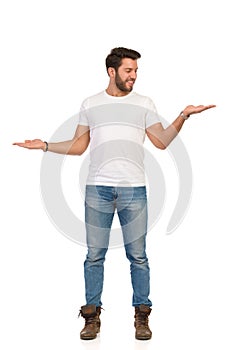 Young Man In Jeans And White T-shirt Is Standing And Compare Something