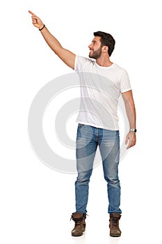 Young Man In Jeans And White T-shirt Is Standing, Smiling And Pointing Up. Front View