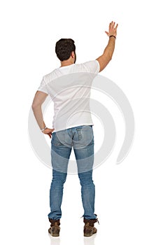 Young Man In Jeans And White T-shirt Is Standing And Waving Hand. Rear View