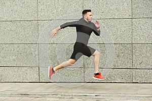 Young man jogging in city against grey urban wall, copy space, side view