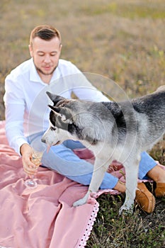 Young man joking with dog and giving glass with wine for dog.
